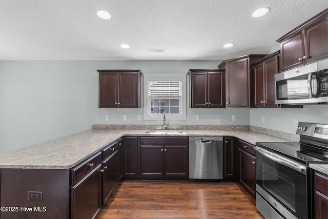 kitchen with dark brown cabinets, a sink, dark wood finished floors, stainless steel appliances, and a peninsula