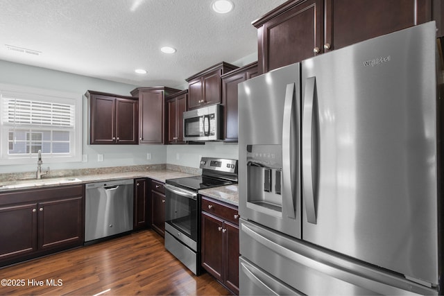 kitchen with a textured ceiling, dark brown cabinets, a sink, light stone counters, and stainless steel appliances