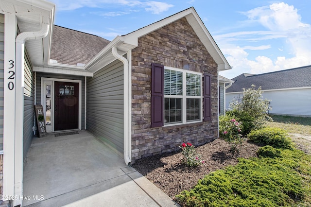 property entrance featuring roof with shingles and stone siding
