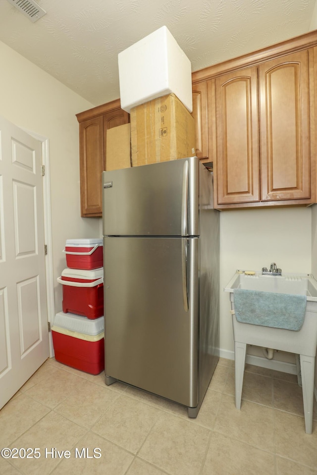 kitchen with visible vents, light tile patterned flooring, freestanding refrigerator, baseboards, and brown cabinetry