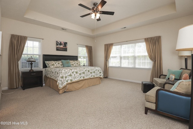 bedroom with a raised ceiling, baseboards, visible vents, and light colored carpet