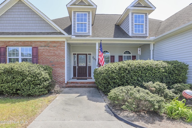 property entrance with brick siding, roof with shingles, and a porch
