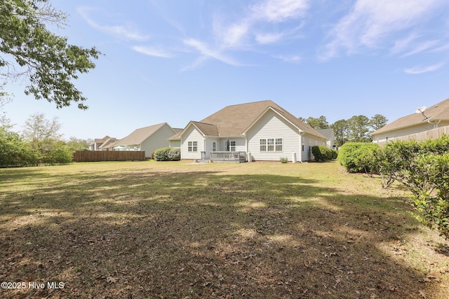 back of property with a wooden deck, a yard, and fence