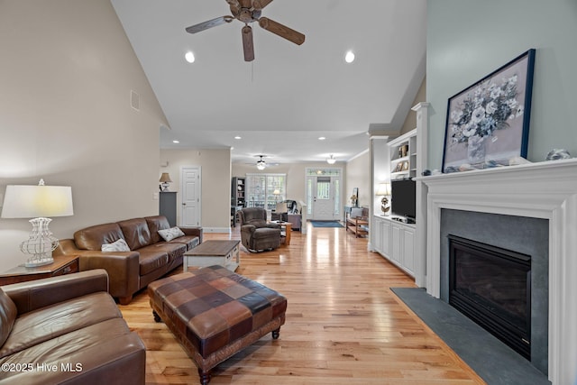 living area with high vaulted ceiling, a fireplace with flush hearth, a ceiling fan, and light wood finished floors