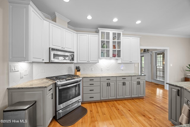 kitchen featuring glass insert cabinets, appliances with stainless steel finishes, tasteful backsplash, and light wood-style flooring