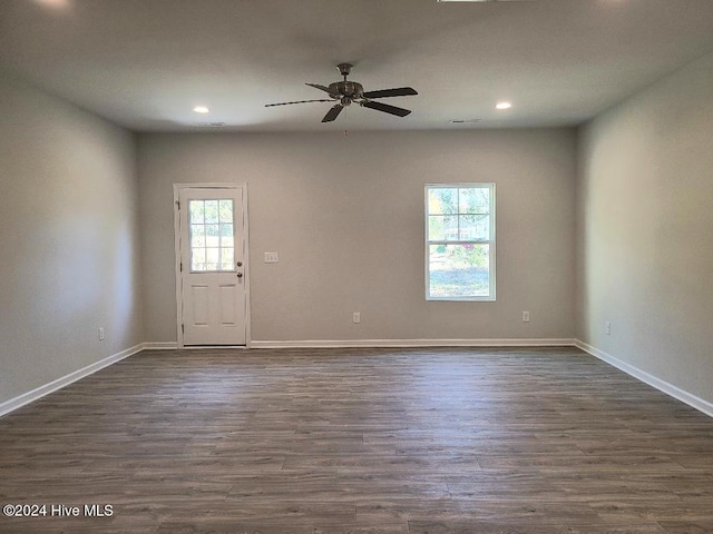 empty room featuring a healthy amount of sunlight, dark wood-style flooring, baseboards, and a ceiling fan
