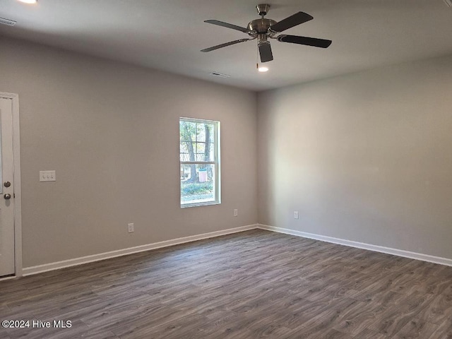 empty room featuring dark wood-type flooring, visible vents, baseboards, and a ceiling fan