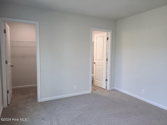 unfurnished bedroom featuring a closet, baseboards, a spacious closet, and carpet floors