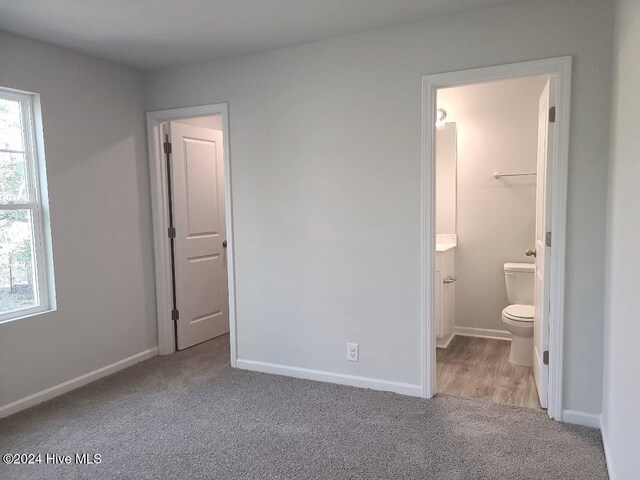 unfurnished bedroom featuring ensuite bathroom, baseboards, and carpet floors