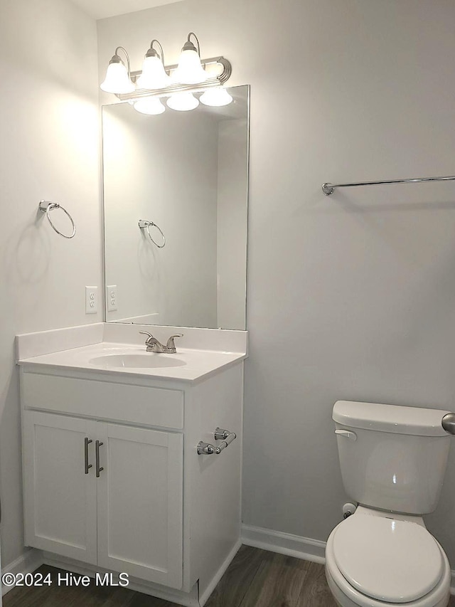 half bathroom with toilet, wood finished floors, vanity, and baseboards