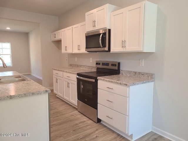 kitchen featuring baseboards, white cabinetry, appliances with stainless steel finishes, light wood finished floors, and a sink