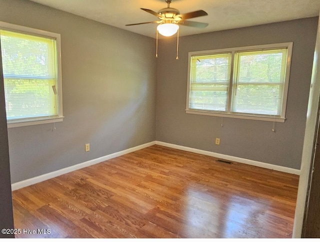 spare room featuring visible vents, ceiling fan, wood finished floors, and baseboards