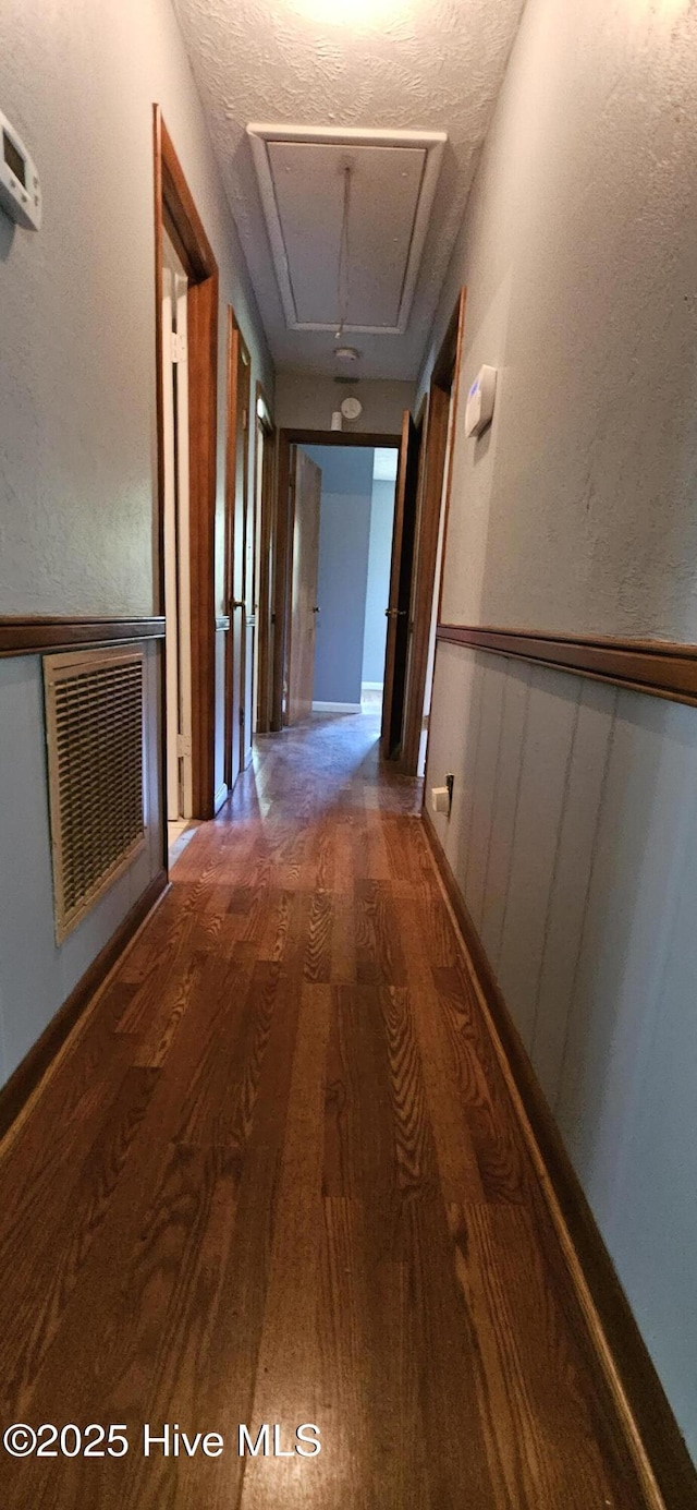 corridor with attic access, visible vents, and wood finished floors