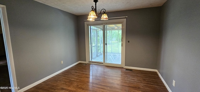 empty room featuring dark wood-style floors, a chandelier, visible vents, baseboards, and a textured ceiling