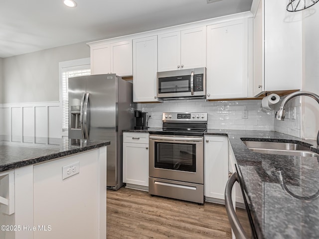 kitchen with white cabinets, stainless steel appliances, a sink, tasteful backsplash, and light wood-style floors