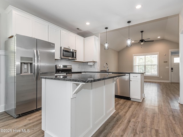 kitchen with light wood finished floors, a peninsula, ceiling fan, a kitchen island, and appliances with stainless steel finishes