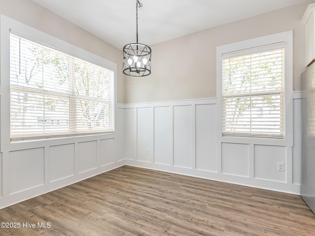 unfurnished dining area featuring a decorative wall, light wood-style flooring, a wainscoted wall, and an inviting chandelier
