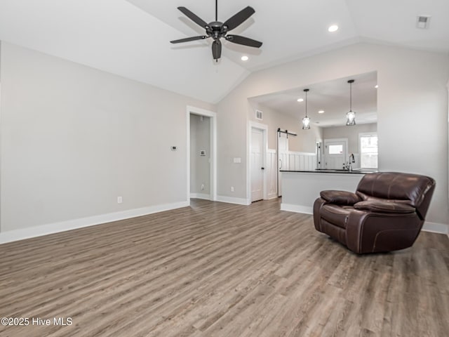 living room featuring lofted ceiling, wood finished floors, ceiling fan, and a barn door