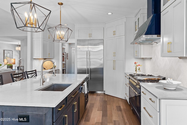 2592 St James Dr SE, Southport, NC 28461 - kitchen featuring high end appliances, wall chimney range hood, a sink, dark wood-style floors, and white cabinetry