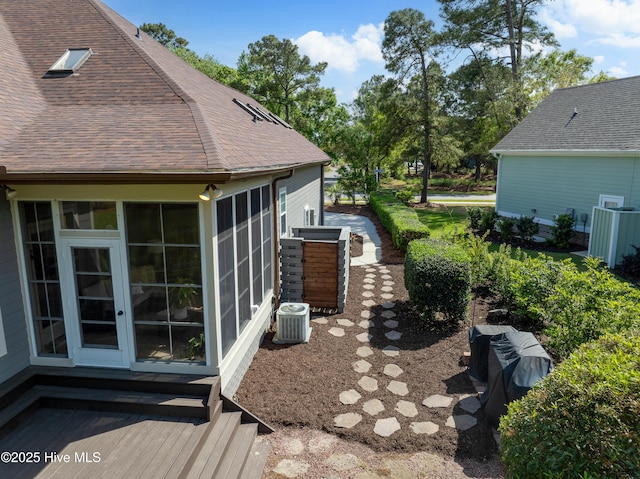 2592 St James Dr SE, Southport, NC 28461 - view of property exterior featuring central AC unit, a shingled roof, a sunroom, and a wooden deck