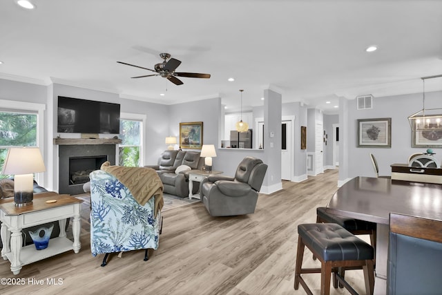 living room with light wood finished floors, visible vents, a ceiling fan, a fireplace, and ornamental molding