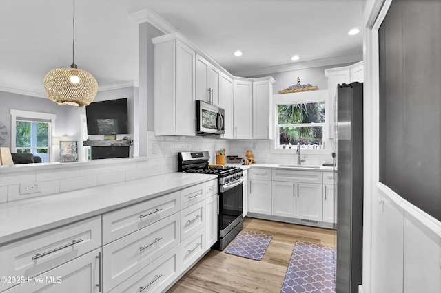 kitchen featuring a sink, light wood-type flooring, white cabinetry, crown molding, and appliances with stainless steel finishes