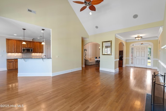 3675 W Medinah Ave, Southport, NC 28461 - unfurnished living room featuring ceiling fan, visible vents, crown molding, arched walkways, and high vaulted ceiling