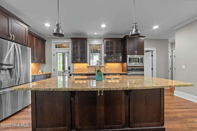 kitchen featuring tasteful backsplash, light stone counters, glass insert cabinets, dark brown cabinets, and stainless steel appliances