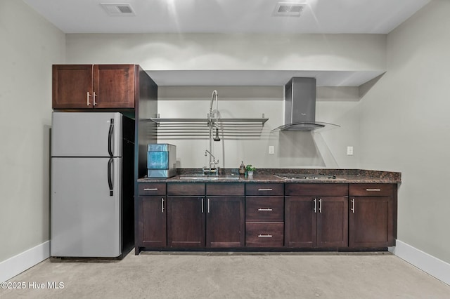 kitchen featuring baseboards, freestanding refrigerator, visible vents, wall chimney exhaust hood, and a sink
