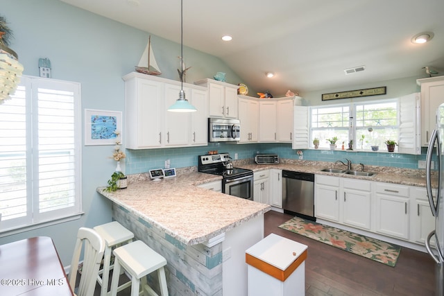 4238 Cherry Laurel Ln SE, Southport, NC 28461 - kitchen with appliances with stainless steel finishes, vaulted ceiling, white cabinets, backsplash, and a peninsula