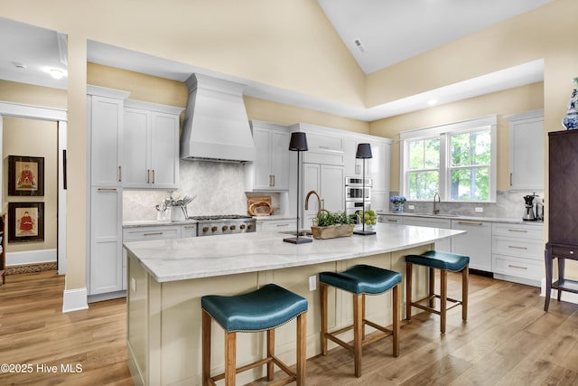 3722 White Cliffs Dr, Castle Hayne, NC 28429 - kitchen with custom exhaust hood, lofted ceiling, a breakfast bar area, light wood-style floors, and stainless steel appliances
