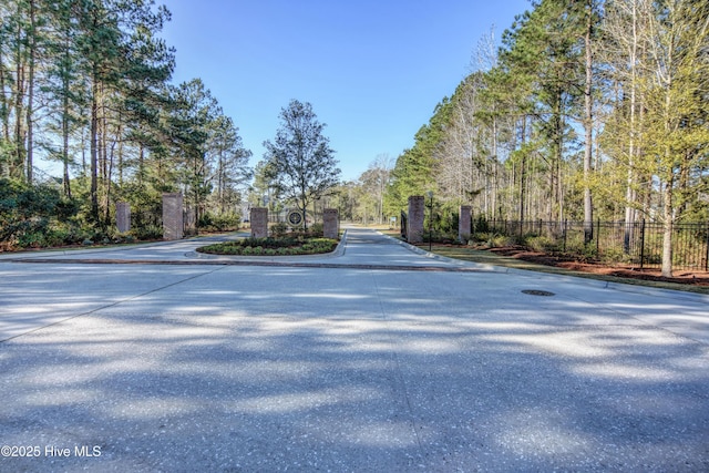 3722 White Cliffs Dr, Castle Hayne, NC 28429 - view of asphalt street with curbs, a gated entry, and a wooded view