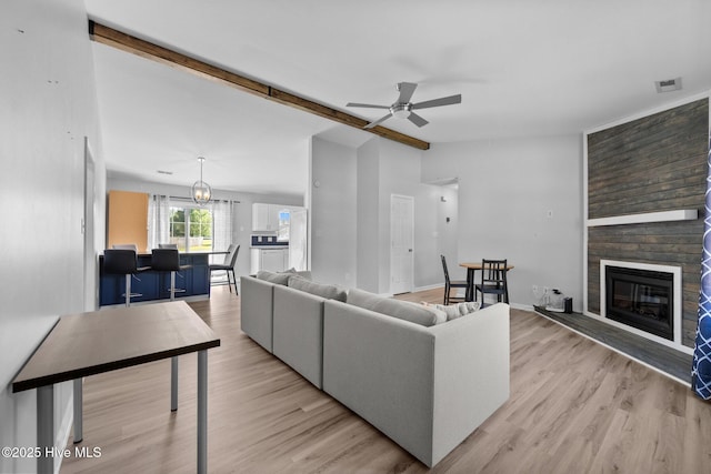 living room featuring lofted ceiling with beams, light wood-style flooring, a ceiling fan, and a fireplace