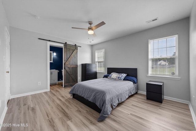 bedroom with baseboards, wood finished floors, visible vents, and a barn door