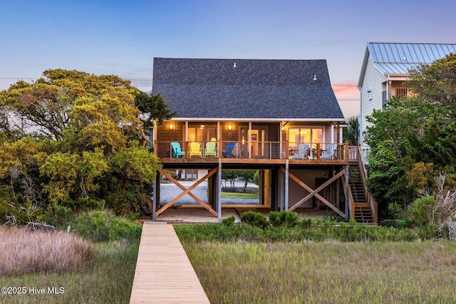 back of property at dusk featuring a deck, a shingled roof, and stairs