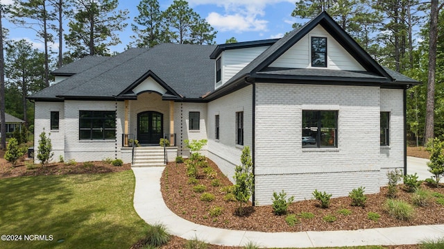 view of front of home with brick siding, french doors, roof with shingles, and a front yard
