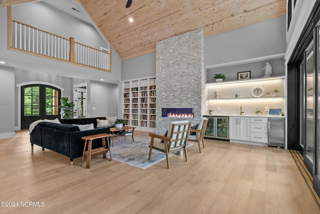 living area featuring high vaulted ceiling, a stone fireplace, light wood-style floors, wood ceiling, and bar area