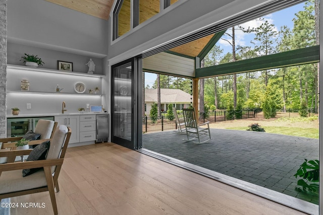 interior space with bar, a sink, light wood-style floors, and high vaulted ceiling