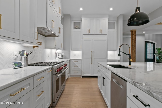 kitchen with white cabinets, light wood-style flooring, a sink, under cabinet range hood, and high quality appliances