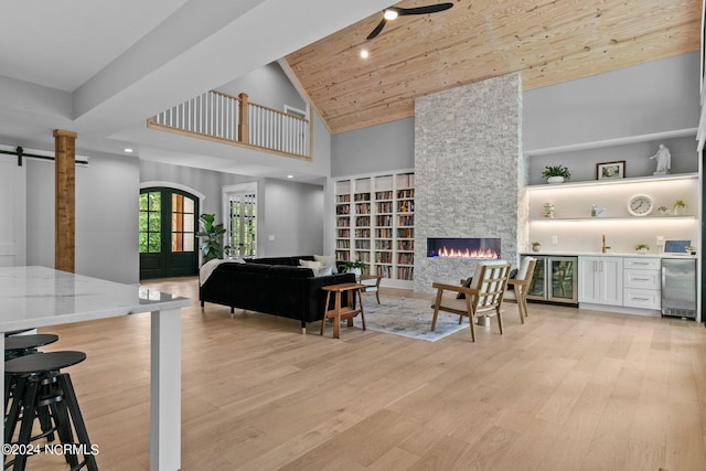 living room with beverage cooler, high vaulted ceiling, a fireplace, light wood-style flooring, and built in shelves