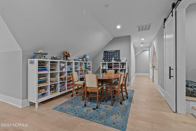 dining space with a barn door, wood finished floors, baseboards, lofted ceiling, and visible vents