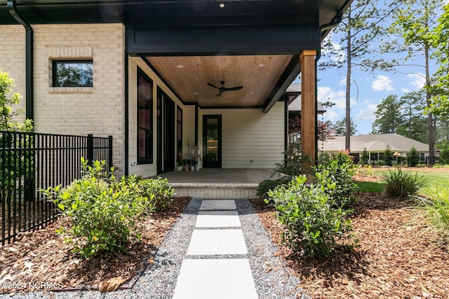 doorway to property featuring fence, a ceiling fan, and brick siding