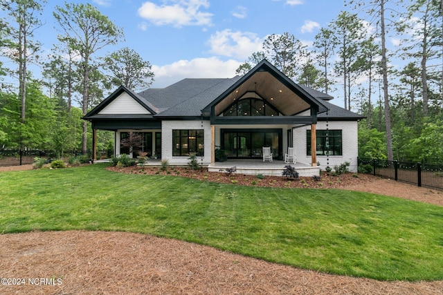 rear view of house with brick siding, a yard, a shingled roof, and fence