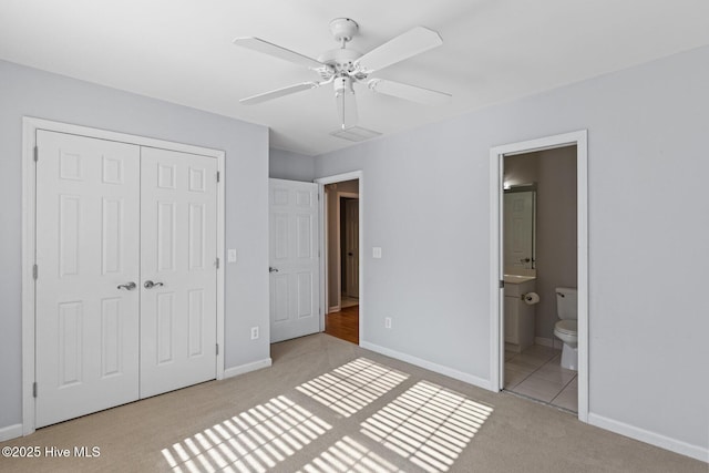 unfurnished bedroom featuring a closet, ensuite bath, a ceiling fan, carpet floors, and baseboards