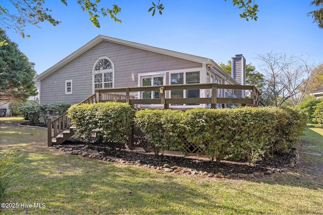 back of house featuring a yard, a wooden deck, and a chimney