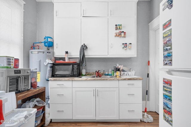 304 Ambler Ave, Rocky Mount, NC 27801 - kitchen with black microwave, white cabinetry, freestanding refrigerator, a sink, and wood finished floors