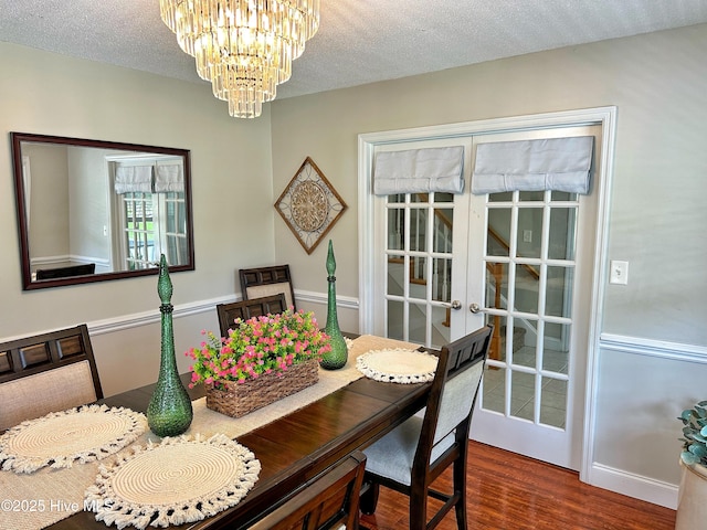 dining area featuring french doors, a textured ceiling, a notable chandelier, and wood finished floors