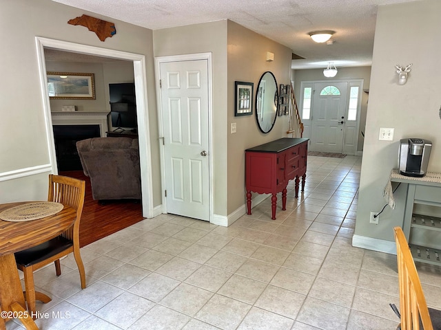 entryway with baseboards, a textured ceiling, light tile patterned floors, and a fireplace