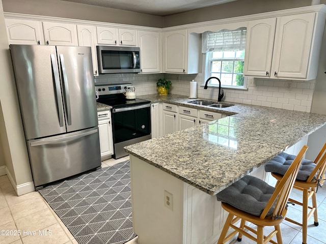 kitchen featuring white cabinets, a sink, stainless steel appliances, a peninsula, and decorative backsplash