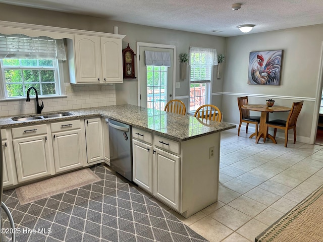 kitchen with a textured ceiling, tasteful backsplash, dishwasher, a sink, and a peninsula